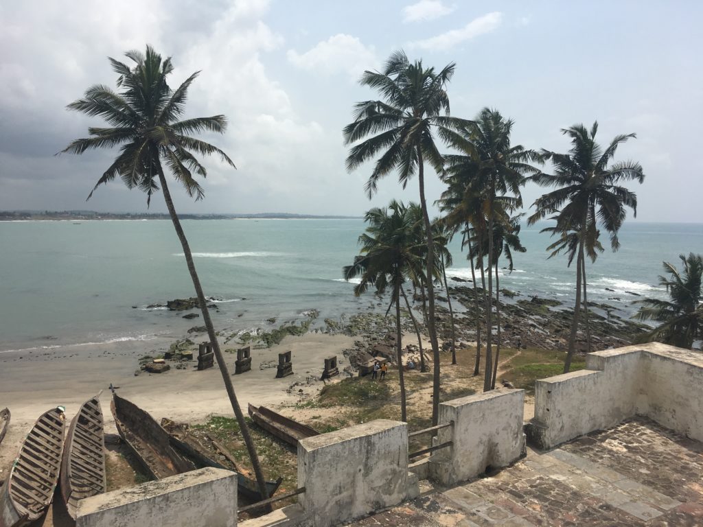 Cheerful palm trees contrast with the history of Elmina Castle. Slave ships used to dock on the sandy shore to carry people to the Americas.